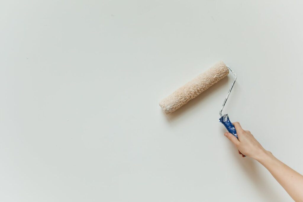 Close-up of a hand painting a wall with a roller brush during renovation.